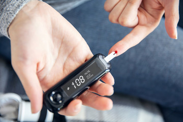 Woman checks her blood glucose level with modern glucometer at home. Interface on the screen was  made in graphic program.