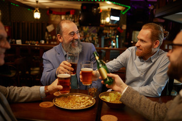 Group of men drinking beer eating snacks and enjoying the conversation while sitting at the table in the pub