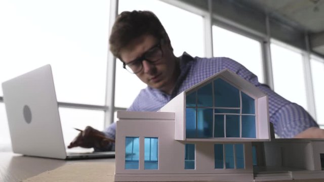 young male architect examing house model