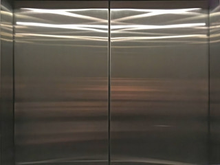 Shiny stainless steel doors of an elevator reflecting the inside ceiling lights
