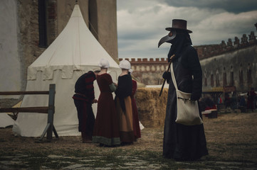 A masquerade historical scene reconstruction. Plague doctor in medieval old town. Castle and...