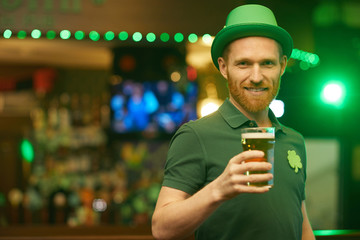 Portrait of young bearded man wearing green hat and holding glass of beer he celebrating St Patrick's Day