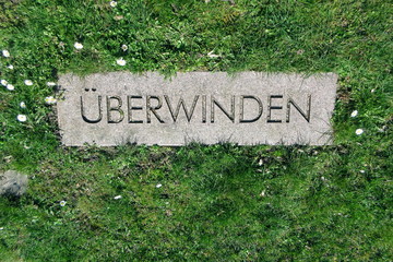 The word - ÜBERWINDEN -  on a memorial stone is a German term and means: TO OVERCOME,  Coronavirus, COVID-19, it's a disaster.