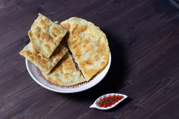 Cheburek and adjika in pots on brown wooden background