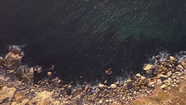 Aerial overhead Ricky coastline and deep ocean at sunset