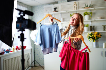 Fashion blogger woman in jeans and turtleneck showing casual colorful shirts on camera. Stylist influencer girl showing trendy clothes filming vlog episode for her channel. Opinion leader sets trends.