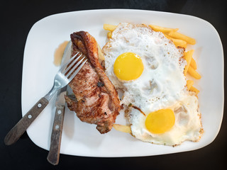 Two fried eggs and meat steak with fork on the white plate