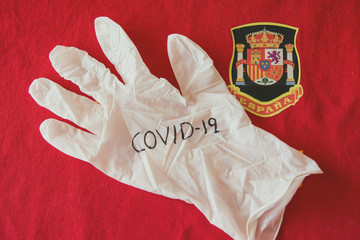 Sanitary glove with the word Covid-19 written on it, on a red background and the Spanish Shield