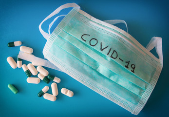 Health mask with the word covid 19 and with medicine pills, on a blue background