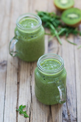 Green drink smoothie with kiwi, banana, spinach and rucola in a jar on a wooden background in ristic style