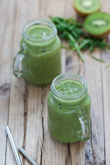 Vegan green drink smoothie with kiwi, banana, spinach and rucola in a jar on a rustic wooden background