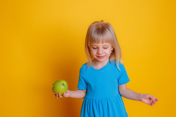 Fototapeta premium baby girl holding a green Apple on a yellow background.