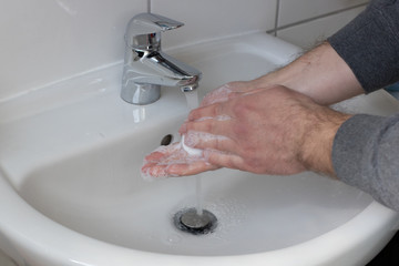 Detail of a Young male washing his Hands with Soap under running water in order to reduce infection Risk during corona Virus pandemic