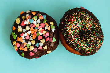 Doughnuts in chocolate glaze with a sprinkle of colored balls and hearts. Delicious dessert for the sweet tooth. Round shape.