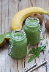 Green smoothie with kiwi, banana, and rucola in a jar on a wooden background in rustic stily