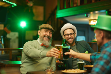 Happy men drinking beer together while celebrating holiday in the pub