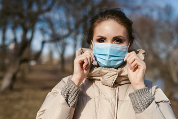 Prevention of coronavirus outbreak in 2020. Outdoor portrait of young european woman wearing a disposable facial mask. Prevent pollution and disease concept.