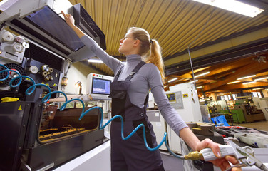 A young woman works as a computerized  numerical control technician. She is seen at her workplace wearing a blue overall. 