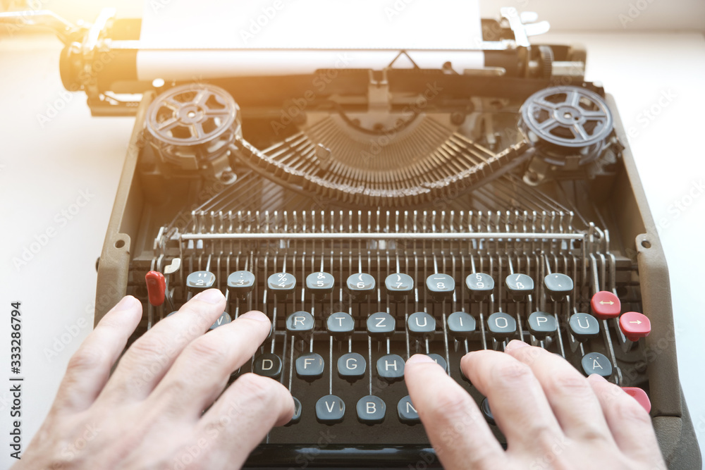 Fototapete fingers type on the keyboard of an old mechanical typewriter in retro style, in the sunlight.