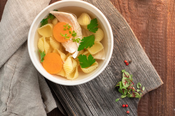 Chicken broth with pasta, carrots, parsley and meat pieces on a wooden background. Homemade soup rustic style