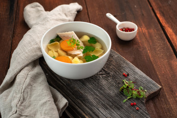 Chicken broth with pasta, carrots, parsley and meat pieces on a wooden background. Homemade soup rustic style