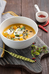 Pumpkin cream soup with seeds and herbs in a white bowl on a wooden background, rustic style