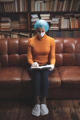 Woman with protective antiviral mask sitting at home in isolation / quarantine and reading book.