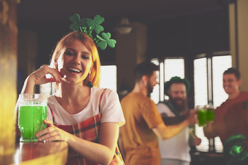 Young woman with glass of green beer in pub, space for text. St. Patrick's Day celebration