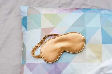 Golden sleeping eye mask on the bed, top view. Good night, flight and travel concept. Sweet dreams, siesta, insomnia, relaxation, tired, travel concept.Do not disturb, mask for sleep, bedtime concept