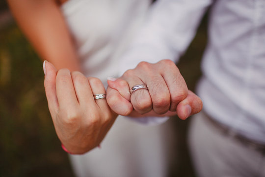 Hands of newlyweds holding each other's little fingers. Wedding rings on your hands