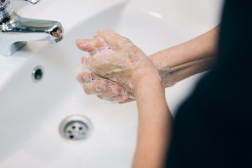 Detail of a woman washing her hands with soap and hot water in a public bathroom. Corona virus pandemic protection