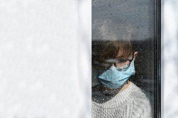 Coronavirus pandemic 2020. Quarantine against infection and spread of the virus COVID-19 concept. Teenager girl in a medical protective mask outside the window in home isolation. rainy day, copy space
