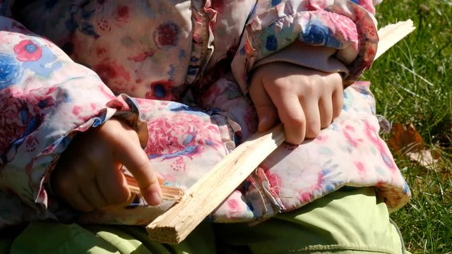 Close-up of midsection of caucasian child girl holding two pieces of wood and scraping them on each other. Seen in Germany in March