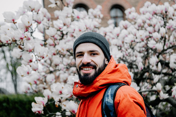stylish young man with beard dressed in spring clothes is photographed near the branches of a blooming magnolia tree