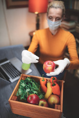 Woman with protective medical mask spraying sterilizing chemical on the food ordered from internet delivery.