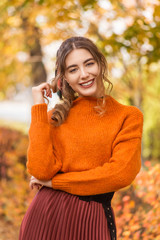 Beautiful young woman on a street in a park in October. The girl is wearing a sweater and pleated skirt. Student teacher is relaxing, walking in the park. Laughs and smiles, cheerful.