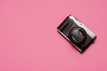 Vintage retro mirrorless camera with lens and lens cap shot from above on a pastel pink background with copy space and room for text with a right side composition