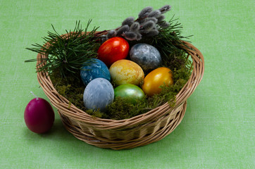Easter, colored painted eggs in a wicker basket with moss and candle