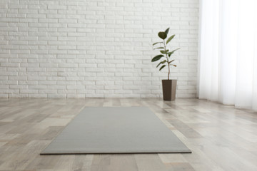 Unrolled grey yoga mat on floor in room - obrazy, fototapety, plakaty