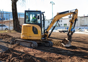 Small yellow excavator is digging ground.