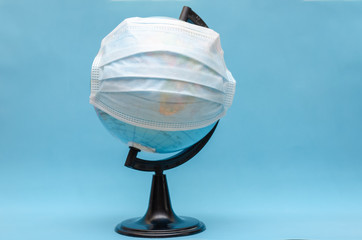 Globe with a medical mask on a blue background with copy space. concept of the coronavirus, infectious diseases