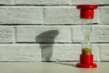 Red glass hourglass close-up against a white brick wall with space. Trend: solar bright light and hard shadows