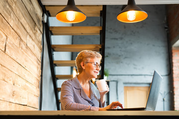 beautiful stylish elderly woman aged sits at a table with a laptop