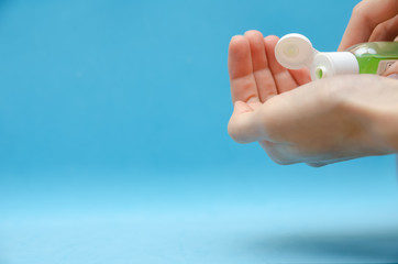 Women's hands using green antibacterial hand gel close up on blue background with copy space