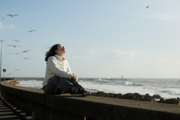 Beautiful asian woman sits on the waterfront during the surf and gulls around.