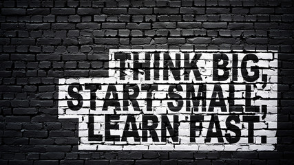 Fototapeta na wymiar Think big, start small, learn fast, motivation and inspiration slogan, white text on black brick wall
