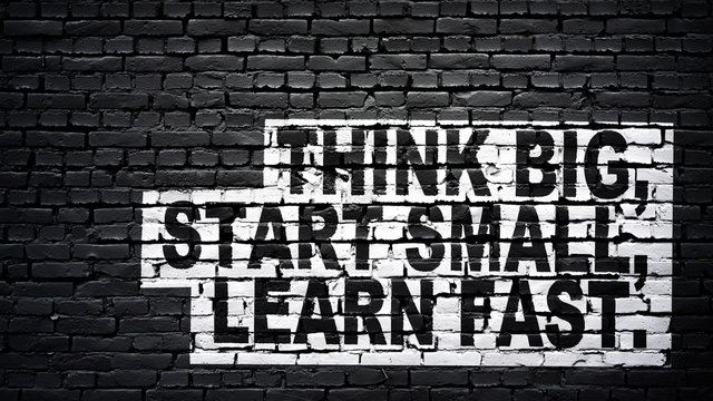 Think big, start small, learn fast, motivation and inspiration slogan, white text on black brick wall