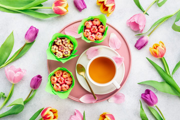 Obraz na płótnie Canvas A cup of tea and cupcakes with tulips on white background