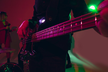 Obraz premium Young and joyful caucasian musician performing on red background in neon light. Concept of music, hobby, festival. Colorful portrait of modern artist. Attented, inspired. Art, cover band. Close up.