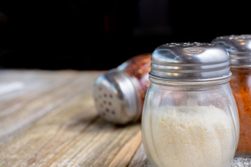 A view of a place setting on a wooden dining table featuring Italian restaurant seasoning, such as parmesan cheese and crushed red pepper.